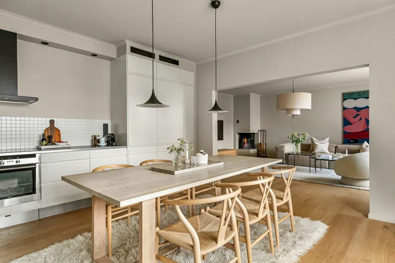 Renovated open-plan living area with a white kitchen, pale timber dining table, wishbone chairs and a lounge beyond